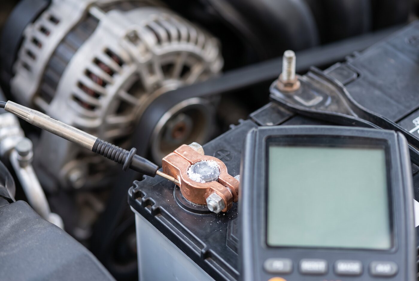 Car battery, terminal clamps and alternator belt in an engine bay